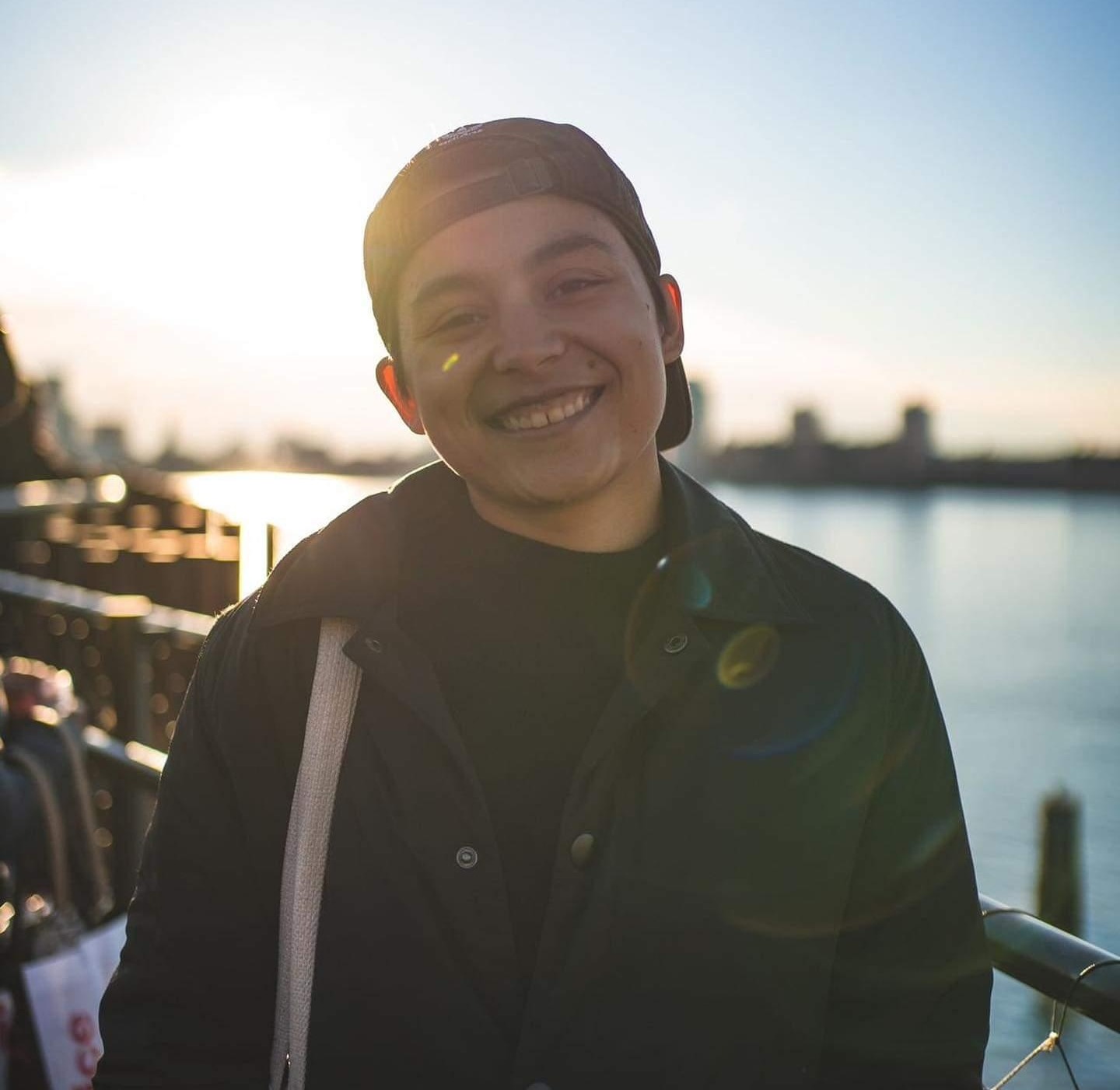 Myself smiling, wearing a black baseball cap backwards, a black sweater, and coat.