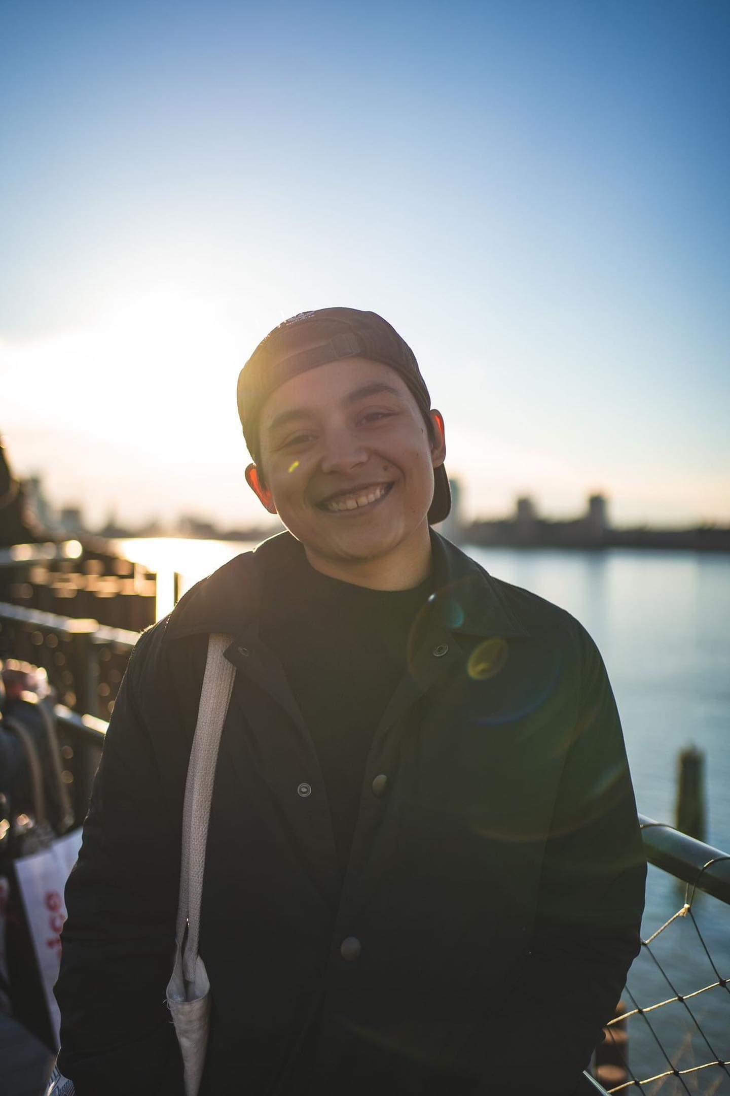 Myself smiling, wearing a black baseball cap backwards, a black sweater, and coat.